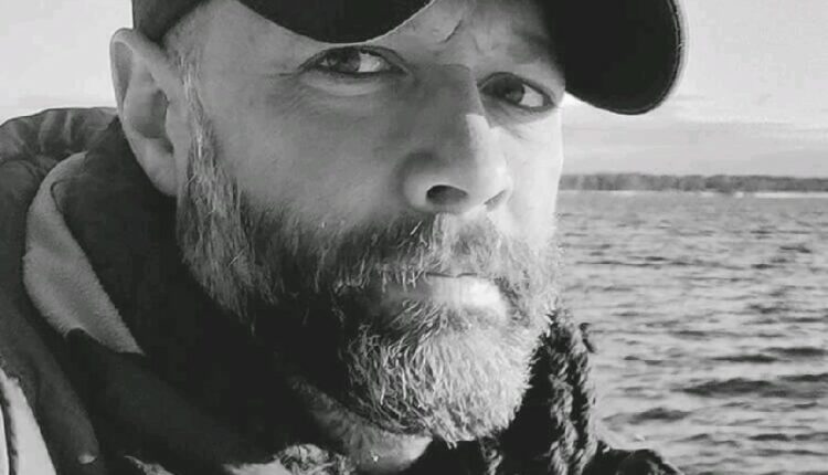 Matthew Knight in a baseball cap and winter jacket sitting near a body of water.