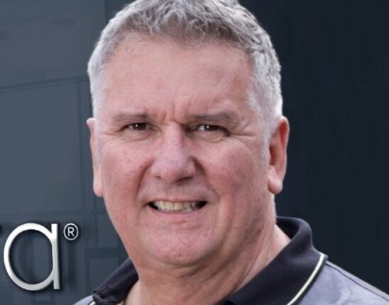 Man with salt and pepper hair wearing a polo t-shirt in front of his office building